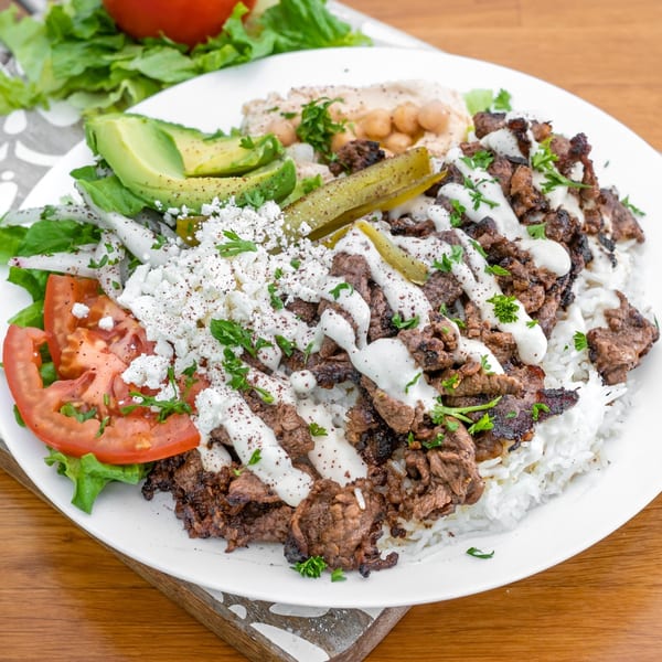 A Falafel California beef shawarma plate with rice, hummus, avocado, feta, and vegetables.