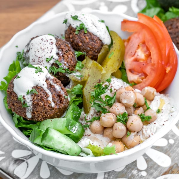 A Falafel California bowl with falafel, hummus, chickpeas, tomatoes, pickles, and lettuce.