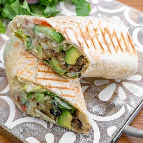 Two halves of a Falafel California wrap filled with avocado, lettuce, and falafel on a wooden board.